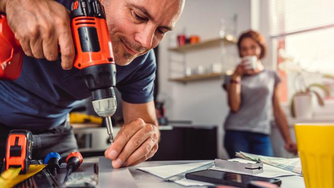 Men renovating kitchen and using cordless drill in the background standing his wife and drinking coffee.