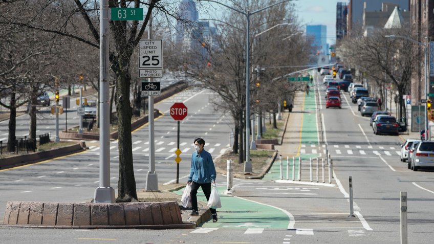 A man wears a mask while carrying groceries across Queens Blvd.