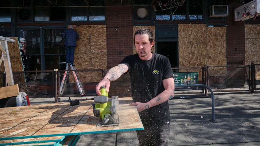 Friend and fellow restaurant owner Brian Patrick saws a piece of plywood while help to board up the windows a pizza restaurant owned by Brian Lee in Seattle, Washington, USA, on 20 March 2020.