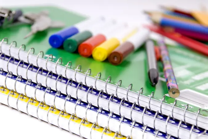Markets, pens, pencil, keys on top of a stack of multicolored notebooks