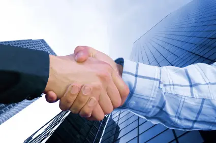 Two business people are standing between high rise buildings, shaking hand and negotiating a deal