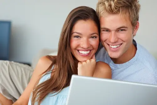 Young happy white couple in front of a laptop